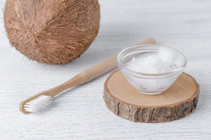 A coconut sitting next to a toothbrush and a glass filled with coconut oil.