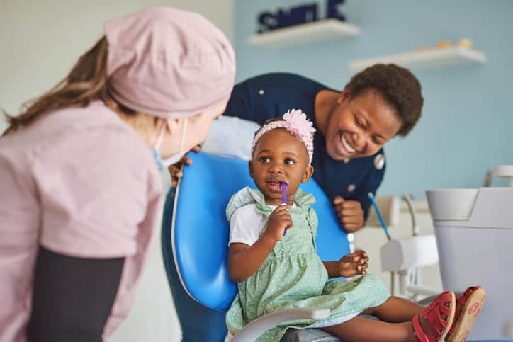 A pediatric dentist sits with her young patient and her mother at the dentist's office. 