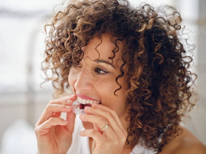 A woman putting in her clear retainer. 