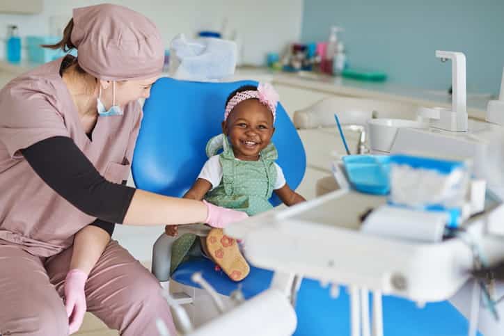 A young girl smiling next to her pediatric dentist. 