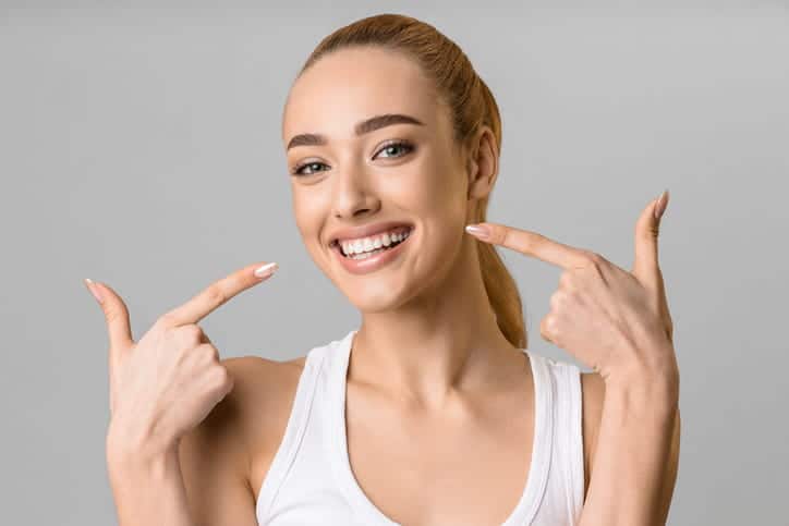 A woman pointing to her smile that shows her gums.