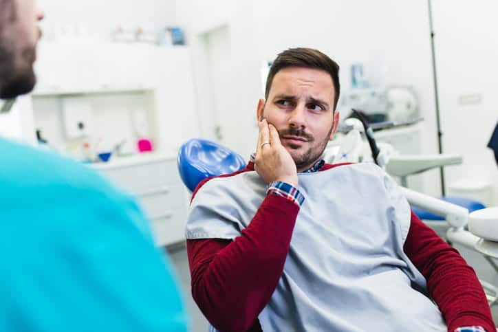 A man holding his jaw in pain as he sees an emergency dentist.