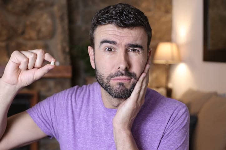 A man holding his face in pain as he holds his lost tooth in his other hand.