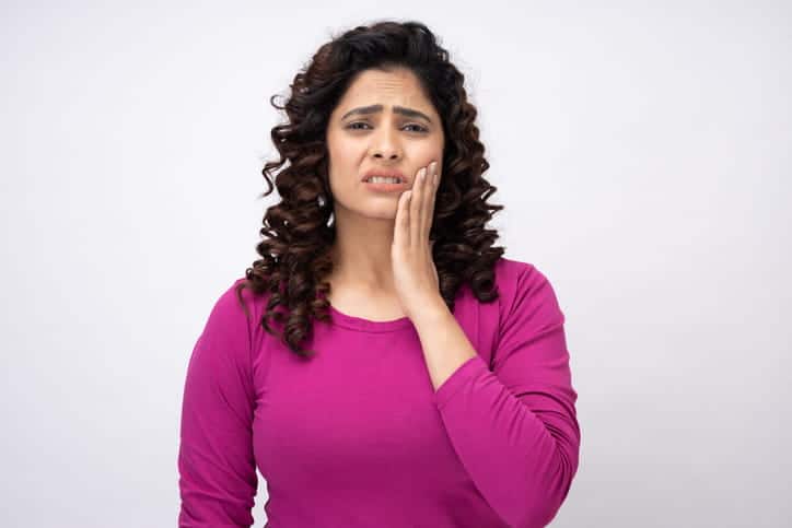 A woman holding her face in pain after experiencing tooth sensitivity.
