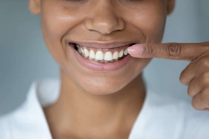 Focus is on a person pointing at their healthy smile after having their teeth cleaned at the dentist.