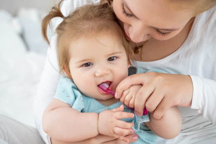 A mother brushing her young child's teeth after their first dental visit.