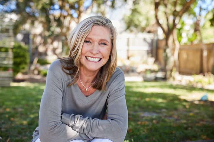 A woman in her backyard smiling.