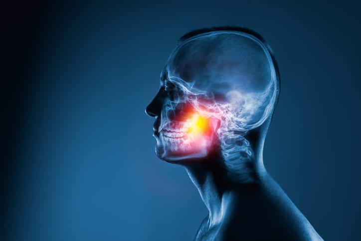An X-ray of a man's head on a blue background. The jaw joint is highlighted by yellow-red color.