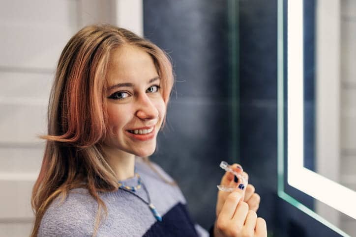 A teenager smiling as she holds her Invisalign tray.