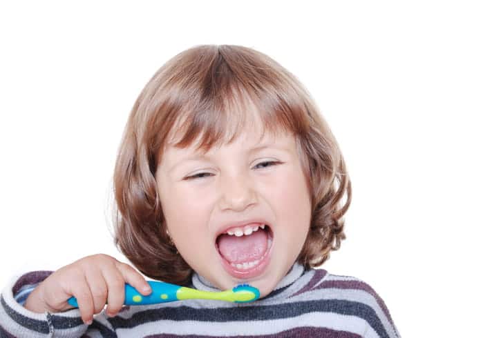 A little kid smiling as they brush their teeth.