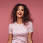 A woman smiling with a pink background behind her.