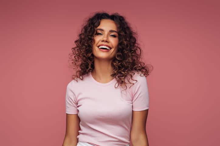 A woman smiling with a pink background behind her.