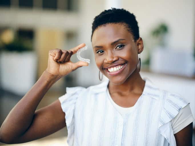 A woman smiling as she holds a clear retainer in her hand.