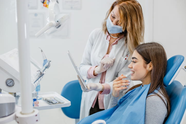 A dentist and a patient both look into a mirror as they look at the patient's teeth.