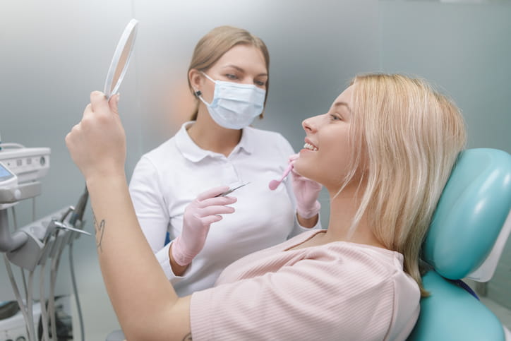 A woman in a dental chair smiles at a mirror as the dentist sits next to her.