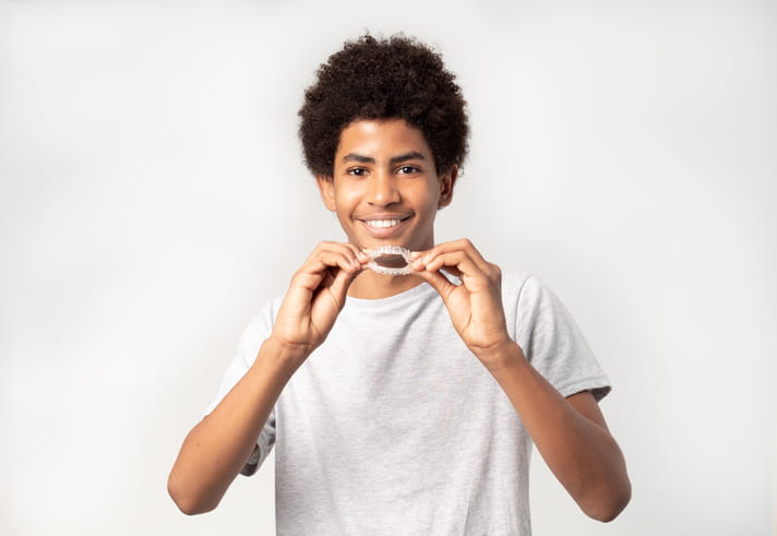 A teenager holding his Invisalign retainers as he smiles.