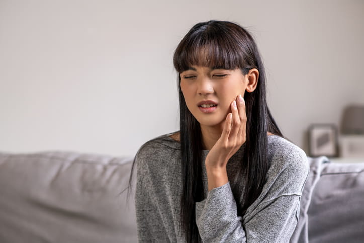 A teenager is holding her jaw in pain from her wisdom teeth coming in.