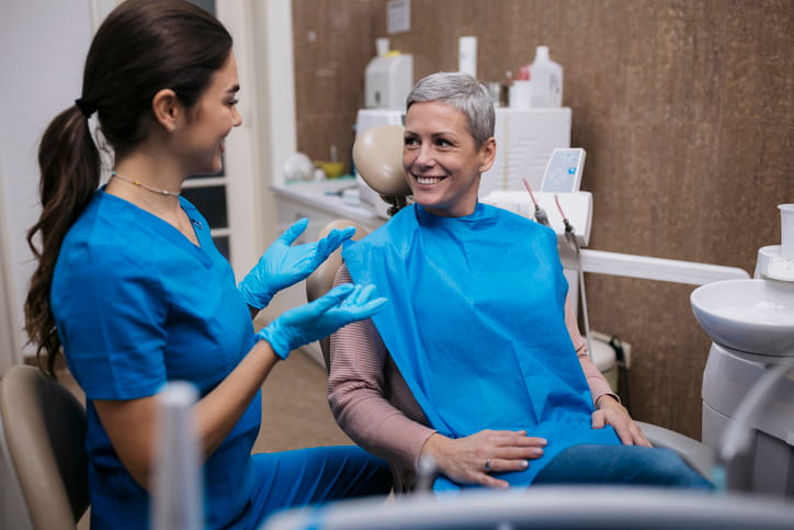 A dental hygienist is smiling as she speaks to her patient about a teeth cleaning.