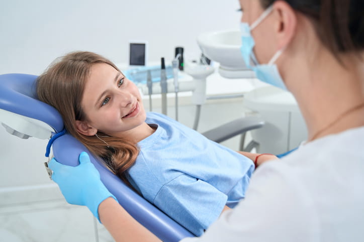 A pedodontist talking to a child who is sitting in a dental chair.